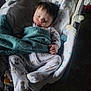baby, sleeping, blanket, pajamas, dog_prints, baby_seat, cushion, colorful_stars, soft_lighting, peaceful, child, infant, cozy, hand, footwear, indoor, portrait, cute, young, resting
