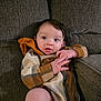 baby, infant, child, plaid_clothing, hooded_outfit, couch, gray_couch, indoor, hands, face, blue_eyes, dark_hair, seated, cozy, cute, portrait, skin, expression, person, casual