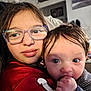 Eddie joined the competition — help win amazing prizes! child, baby, glasses, red_jersey, indoor, portrait, close_up, face, curly_hair, hand, couch, person, young, sibling, cute, expression, clothing, blue_eyes, hair, home