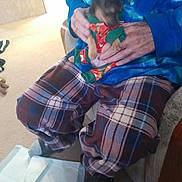 Dakota joined the competition — help win amazing prizes! blue_shirt, blurred_face, carpet, casual, chair, cozy, dog, footwear, furniture, hands, holding, home, indoor, pajamas, person, pet_clothing, plaid_pants, puppy, slipper, sock