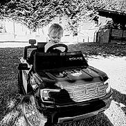Marceau a rejoint le concours — aidez-le/la à gagner de superbes lots ! black_and_white, car_toy, child, daylight, fun, grass, happy, nature, outdoor, park, play, police_car, small_building, smiling, steering_wheel, toddler, toy_car, trees, vehicle, young_child
