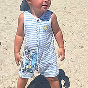 Bastien a rejoint le concours — aidez-le/la à gagner de superbes lots ! toddler, child, beach, sand, sunny, cap, romper, striped_clothing, cartoon_character, barefoot, summer, outdoor, young_child, cute, sunlight, shadow, playful, vacation, fun, sand_on_hands