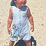 toddler, child, beach, sand, sunny, cap, romper, striped_clothing, cartoon_character, barefoot, summer, outdoor, young_child, cute, sunlight, shadow, playful, vacation, fun, sand_on_hands