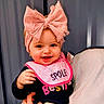 baby, child, smiling, pink_bow, bib, clothing, person, portrait, happy, hand, headwear, indoor, cute, young_child, apparel, face, infant, expression, cheerful, holding