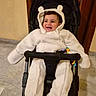 baby, child, clothing, cozy, cute, door, ears, happy, hood, indoor, infant, marble_floor, person, seat, smiling, stroller, toy, warm_clothing, white_bear_suit, wooden_door