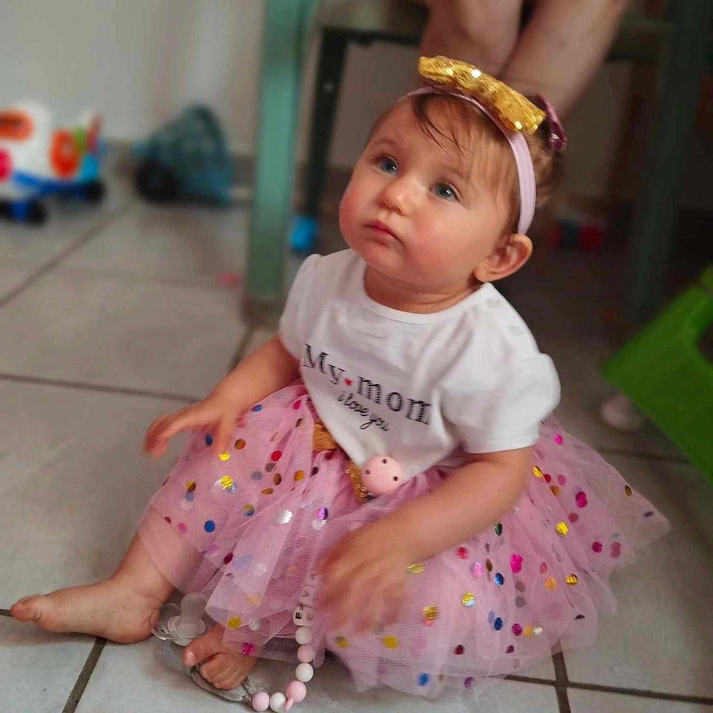 Eva participe au concours pour gagner de l'argent avec cette photo : accessories, baby, bodypart, bracelet, clothing, dress, face, finger, footwear, hand, head, jewelry, pants, person, photography, portrait, sandal, sitting, skirt, sleeve