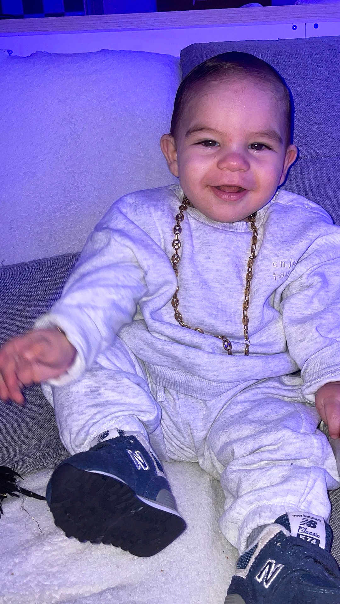 Kaëlan participe au concours pour gagner de l'argent avec cette photo : baby, blanket, candid, casual_clothing, cheeks, child, couch, face, footwear, gold_chain, happy, indoor, new_balance, portrait, purple_light, sitting, smile, sneakers, sweatshirt, toddler
