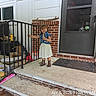 toddler, child, dress, denim_vest, boots, porch, stairs, railing, brick_wall, door, window, concrete, smiling, outdoor, handrail, steps, person, clothing, daylight, front_porch