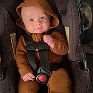 River is registered to the contest to win money with this photo: baby, car_seat, hooded_outfit, straps, infant, clothing, seat_belt, child, cute, indoor, person, blue_socks, smiling, face, young_child, car_seat_padding, baby_clothes, sitting, safety_harness, hood