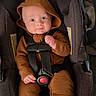 baby, car_seat, hooded_outfit, straps, infant, clothing, seat_belt, child, cute, indoor, person, blue_socks, smiling, face, young_child, car_seat_padding, baby_clothes, sitting, safety_harness, hood