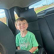 Wayln is registered to the contest to win money with this photo: child, boy, smiling, green_tshirt, car_seat, backseat, vehicle_interior, window, rural_landscape, field, power_lines, sky, seatbelt, headrest, casual_clothing, portrait, happy, daytime, transportation, young