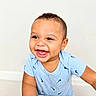 baby, toddler, child, smiling, happy, face, person, blue_shirt, short_sleeve, indoor, cute, joyful, small_child, leaning, light_background, portrait, expressive, curly_hair, skin, photography