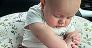Bodie is registered to the contest to win money with this photo: baby, infant, child, car_seat, car_interior, hand, clothing, pants, shirt, bald_head, cute, sitting, holding_hands, support, window, greenery, indoors, seat, portrait, young