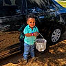 Axl James is registered to the contest to win money with this photo: black_car, boy, bucket, car, casual_clothing, child, daylight, happy, jeans, nature, outdoor, pine_needles, playful, portrait, reflection, shirt, shoes, standing, toddler, watch