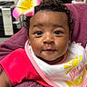 baby, infant, child, curly_hair, flower, pink, yellow, bib, red_clothing, blanket, portrait, smiling, indoors, cute, face, person, young_child, happy, closeup, headshot