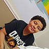 arm, background, boy, casual_clothing, child, colorful, curly_hair, graphic_tee, happy, indoor, light, person, portrait, rainbow_paint, room, seated, smiling, tshirt, wall, young