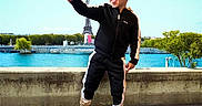Yanis is registered to the contest to win money with this photo: child, boy, sunglasses, tracksuit, sneakers, pointing, outdoor, eiffel_tower, landmark, river, concrete_wall, trees, blue_sky, happy, smiling, fashion, urban, daylight, person, portrait