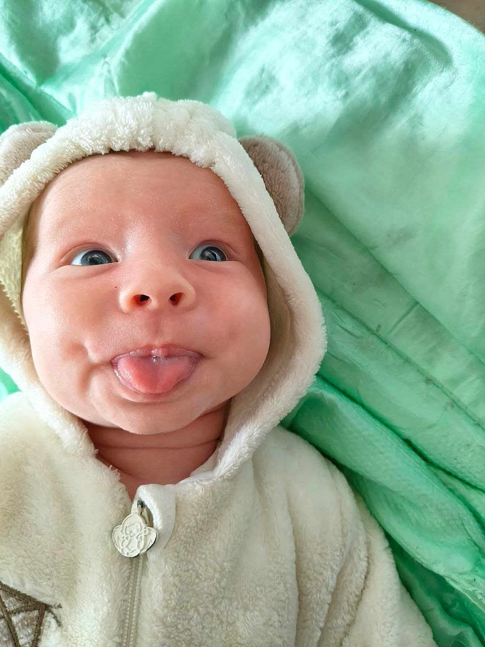 Lucian participe au concours pour gagner de l'argent avec cette photo : baby, infant, tongue_out, hoodie, soft, blanket, cute, face, expression, smile, blue_eyes, close_up, child, wearing_clothes, warm, indoor, portrait, baby_clothing, funny_face, playful