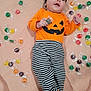 Arabella is registered to the contest to win money with this photo: baby, black_and_white, black_headband, blanket, bow, candy, child, colorful, costume, cute, footwear, halloween, indoors, infant, lying_down, orange_shirt, pumpkin_face, smile, striped_pants, wrapped_candy