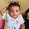 baby, child, smiling, sitting, indoor, clothing, pink_chair, sunglasses, star_pattern, cute, portrait, happy, person, infant, short_hair, casual, playful, expression, light_background, hand_up