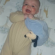 Layne joined the competition — help win amazing prizes! baby, child, onesie, blanket, plush_toy, giraffe_pattern, bedspread, smile, happy, infant, cute, face, hand, blue_blanket, animal_print, sleepwear, lying_down, indoors, person, young_child