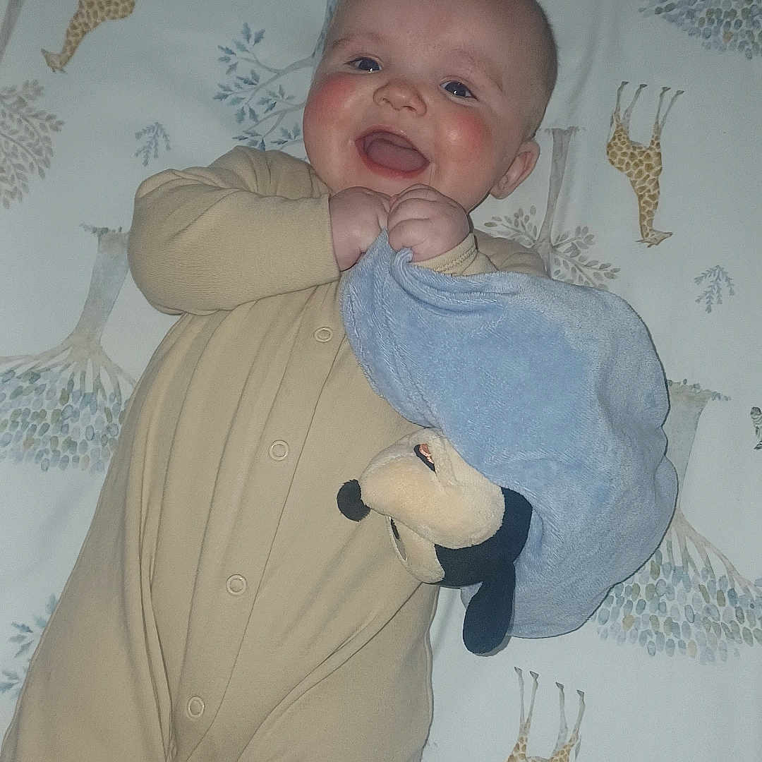 Layne joined the competition — help win amazing prizes! animal_print, baby, bedspread, blanket, blue_blanket, child, cute, face, giraffe_pattern, hand, happy, indoors, infant, lying_down, onesie, person, plush_toy, sleepwear, smile, young_child