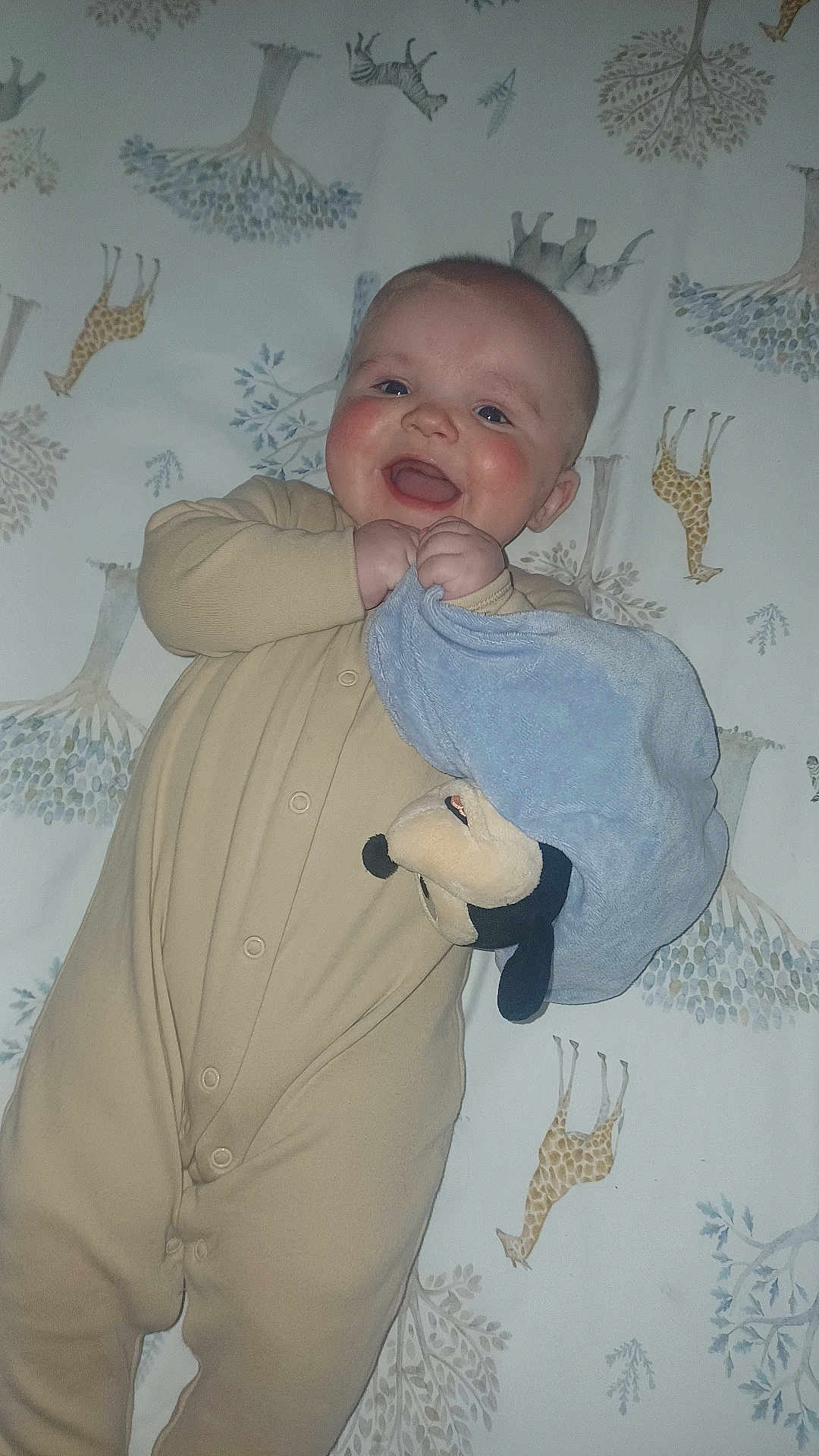 Layne joined the competition — help win amazing prizes! baby, child, onesie, blanket, plush_toy, giraffe_pattern, bedspread, smile, happy, infant, cute, face, hand, blue_blanket, animal_print, sleepwear, lying_down, indoors, person, young_child