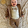 baby, infant, smiling, happy, face, eyes, mouth_open, baby_clothes, shirt_with_text, boss_shirt, hoodie, joggers, socks, blanket, quilt, wooden_milestone, six_months, lying_down, portrait, neutral_tones