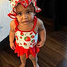 Ayla is registered to the contest to win money with this photo: barefoot, bed, child, clothing, curious_expression, cute, dark_curtains, indoors, looking_up, person, portrait, red, standing, strawberry_pattern, summer_wear, sunhat, swimsuit, toddler, white, wooden_floor