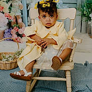 Ayla is registered to the contest to win money with this photo: toddler, child, yellow_coat, floral_dress, wooden_chair, keys, curly_hair, hair_bows, stuffed_bunny, basket, flowers, indoor, portrait, cute, curious, floor_rug, decor, baby_sandals, seated, expression