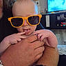 Isaiah joined the competition — help win amazing prizes! baby, infant, child, sunglasses, orange_glasses, portrait, smiling, indoor, held, hands, family, parent, living_room, television, furniture, home, close_up, cute, fashionable, funny