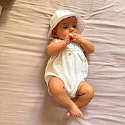 Julia joined the competition — help win amazing prizes! baby, infant, white_clothing, hat, bed, blanket, skin, hands, feet, lying_down, indoors, curious, cute, small, child, one_person, minimalist, soft_light, peaceful, portrait