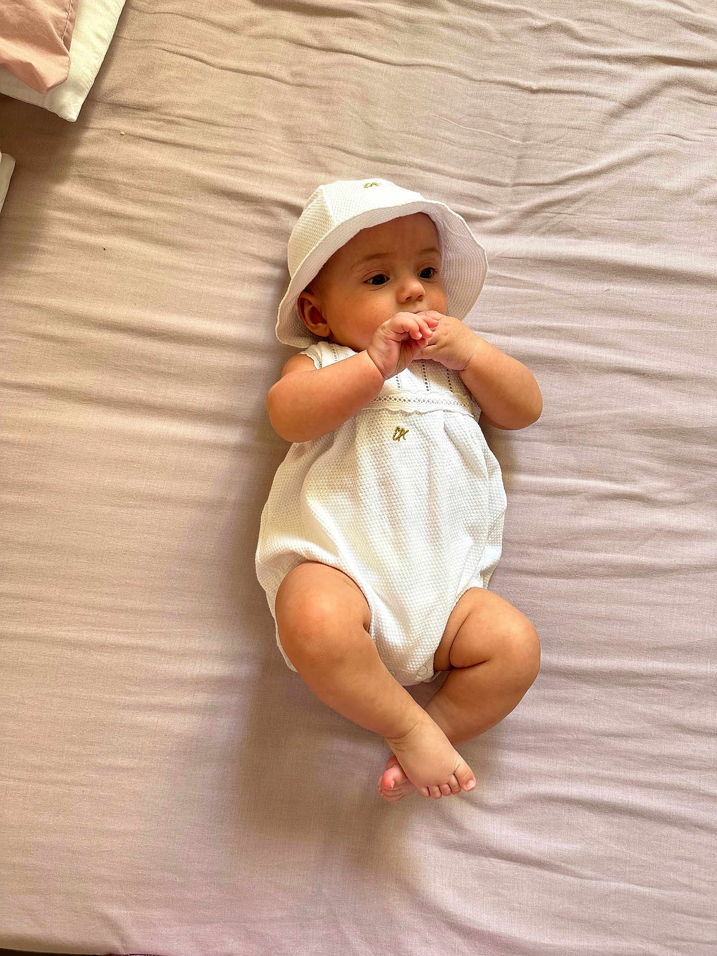 Julia joined the competition — help win amazing prizes! baby, infant, white_clothing, hat, bed, blanket, skin, hands, feet, lying_down, indoors, curious, cute, small, child, one_person, minimalist, soft_light, peaceful, portrait