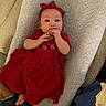 baby, infant, red_dress, headband, cushion, hand, fingers, feet, indoor, person, child, cute, lying_down, fabric, texture, floor, wood_floor, clothing, portrait, relaxing