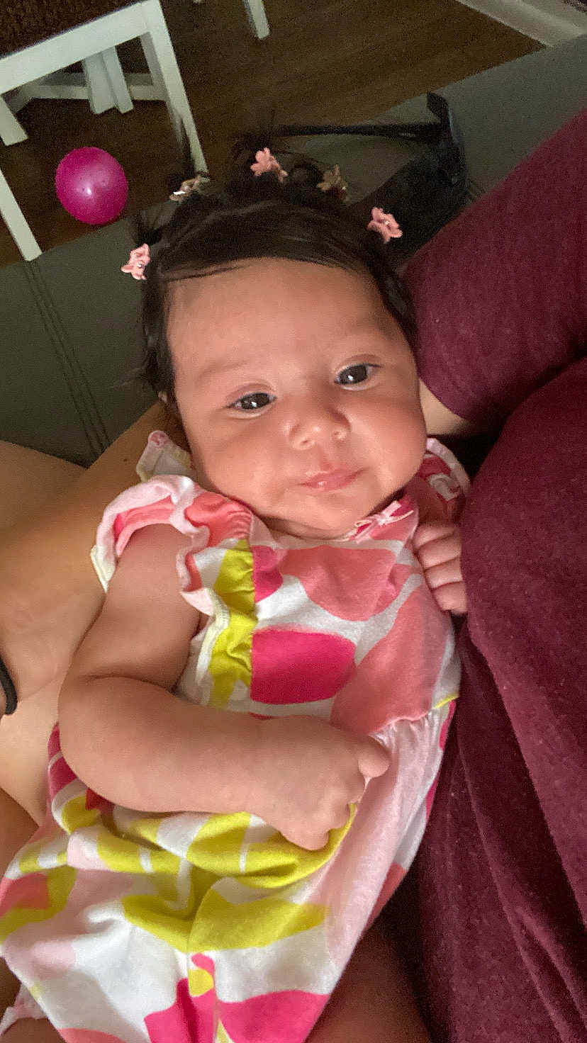 Nayeli is registered to the contest to win money with this photo: baby, child, infant, girl, dress, pink, hair_clips, arms, person, indoor, balloon, colorful, patterned_clothing, closeup, cute, smile, skin, face, holding, relaxed