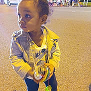 Khaycee is registered to the contest to win money with this photo: child, toddler, denim_jacket, boots, street, night, toy, people, building, signage, sidewalk, outdoor, curious, holding, jewelry, casual_clothing, young_child, urban, pavement, lights
