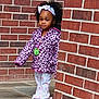 Khaycee joined the competition — help win amazing prizes! child, toddler, girl, brick_wall, jacket, headband, curly_hair, outdoor, sidewalk, patterned_clothing, purple, white, peeking, young_child, cute, fashion, casual, portrait, standing, expression