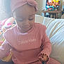 toddler, child, pink_clothing, headband, smiling, indoor, couch, toy, television, curly_hair, person, cozy, home, furniture, casual, sitting, young_child, happy, playful, relaxed