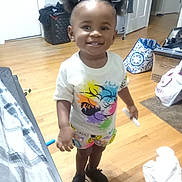 Kalani is registered to the contest to win money with this photo: bag, box, casual_wear, child, colorful_clothing, door, earrings, floor, hair_bows, happy, indoor, laundry_basket, person, room, shoes, smiling, standing, toddler, toy, wooden_floor