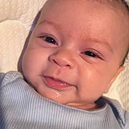 Josiah is registered to the contest to win money with this photo: baby, infant, smile, face, blue_onesie, dinosaur_print, closeup, cute, child, newborn, soft_cushion, happy, skin, eyes, portrait, young, baby_clothing, lying_down, indoors, person