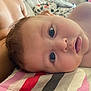 baby, infant, face, blue_eyes, skin, closeup, blanket, striped, lying_down, person, adult, torso, curious, expression, indoors, soft_light, cheeks, nose, mouth, hair
