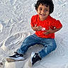 child, smiling, sand, red_shirt, jeans, sneakers, outdoor, happy, curly_hair, casual_clothing, playful, sitting, footwear, nature, daylight, portrait, young_child, joyful, fun, casual
