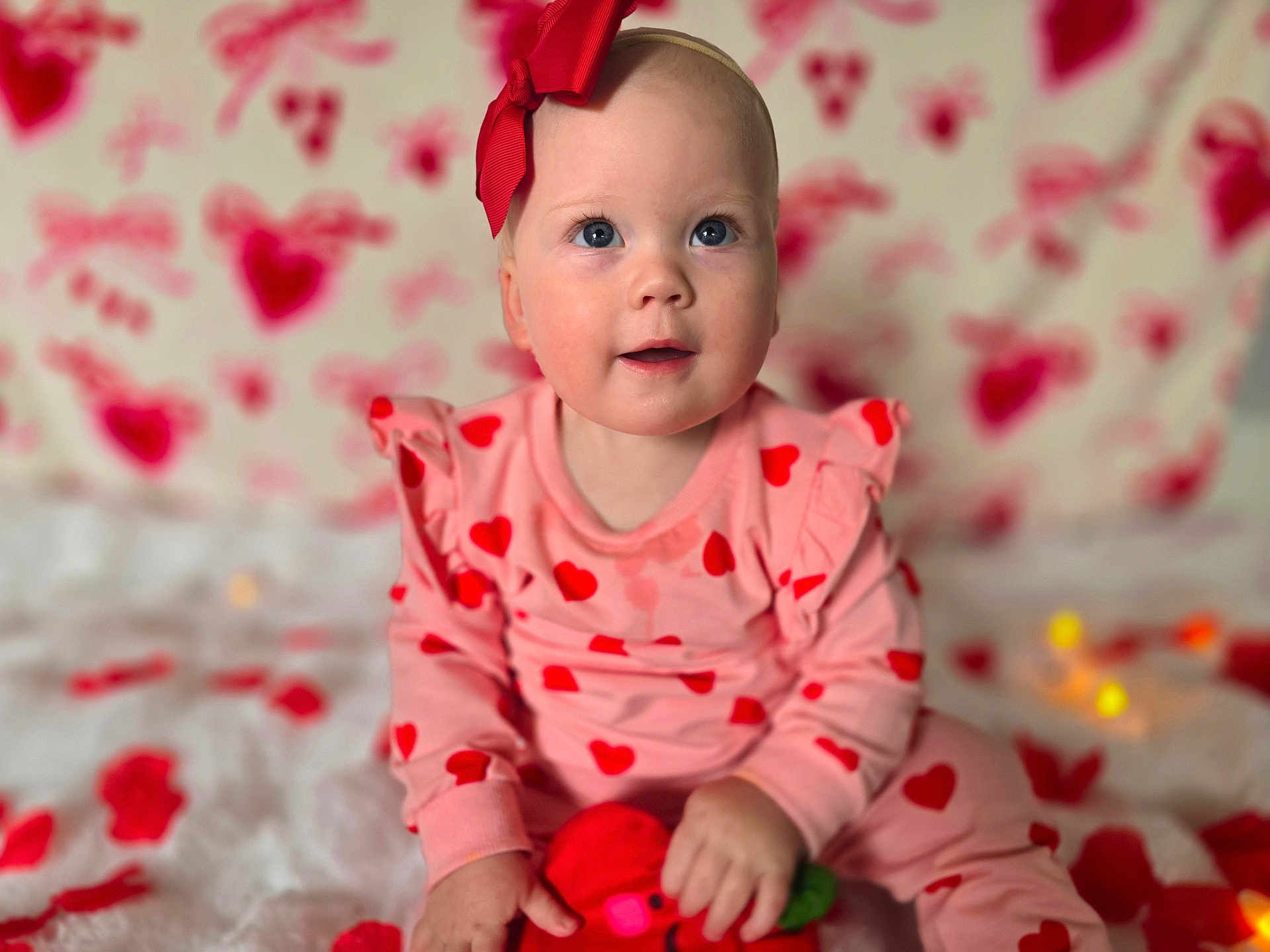 Lily joined the competition — help win amazing prizes! baby, infant, child, bow, headband, hearts_pattern, pink_clothing, sitting, plush_toy, blanket, portrait, adorable, blue_eyes, rosy_cheeks, smile, soft_lighting, shallow_depth, bokeh, indoor, valentine_theme
