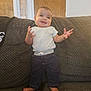 baby, child, smile, couch, clothing, white_shirt, dark_pants, barefoot, indoors, furniture, height_ruler, wooden_door, home, person, happy, standing, texture, cute, infant, expression