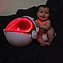 baby, child, diaper, smiling, helmet, red_light, glowing, futuristic, couch, dark_background, indoor, sitting, happy, toy, technology, face, person, infant, home, play