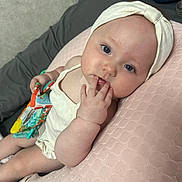 Laylah is registered to the contest to win money with this photo: baby, infant, headband, blue_eyes, hand, fingers, toy, pillow, pink, cream_clothing, bedding, lying_down, cute, child, skin, face, expression, indoor, soft_texture, curious
