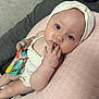baby, infant, headband, blue_eyes, hand, fingers, toy, pillow, pink, cream_clothing, bedding, lying_down, cute, child, skin, face, expression, indoor, soft_texture, curious