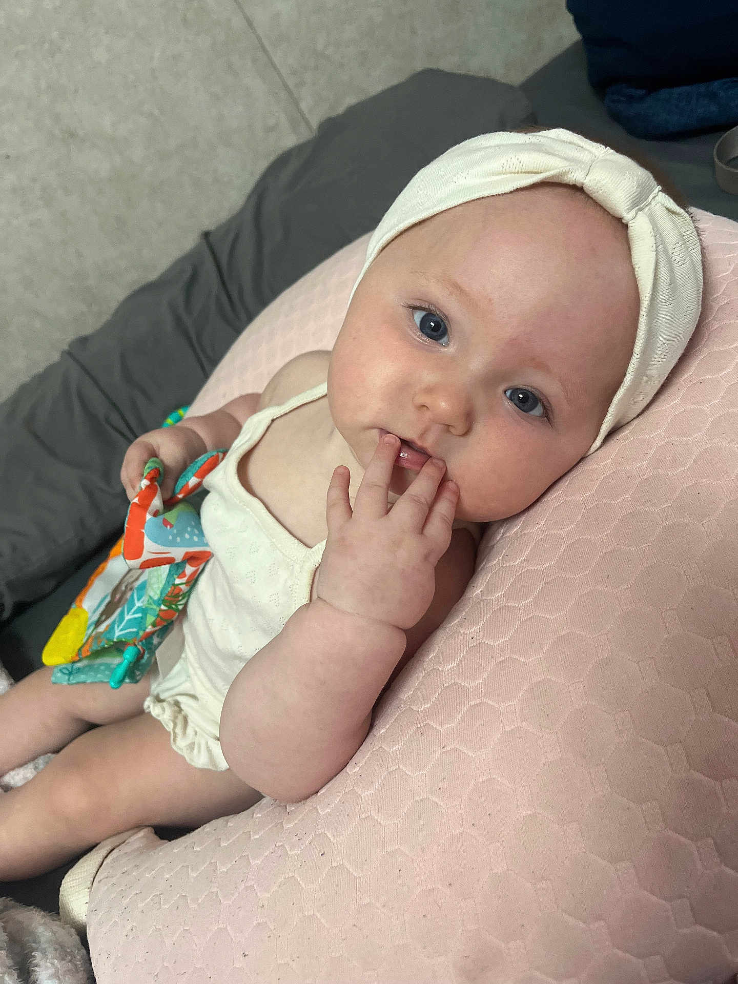 Laylah is registered to the contest to win money with this photo: baby, infant, headband, blue_eyes, hand, fingers, toy, pillow, pink, cream_clothing, bedding, lying_down, cute, child, skin, face, expression, indoor, soft_texture, curious