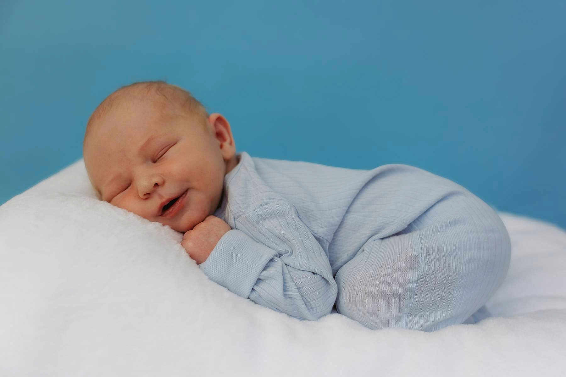 Walker is registered to the contest to win money with this photo: baby, newborn, sleeping, pajamas, blue_background, soft_texture, white_blanket, peaceful, closeup, infant, cute, resting, child, portrait, sleep, cozy, toddler, face, skin, relaxation