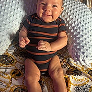 Legend is registered to the contest to win money with this photo: baby, infant, smile, striped_clothing, onesie, pillow, patterned_blanket, tiger_design, golden_chains, sitting, cute, happy, indoor, young_child, face, legs, hands, black_socks, texture, soft